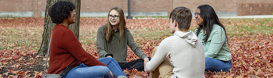 photo of four students sitting outside on campus