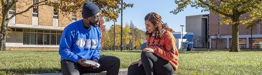photo of two students sitting outside on campus